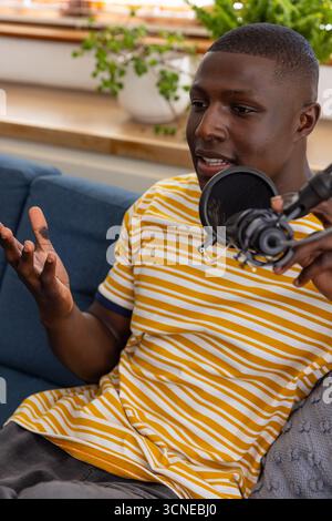 afroamerikaner, der auf blauer Couch in Popfilter-Mikrofon spricht, Gesten Stockfoto