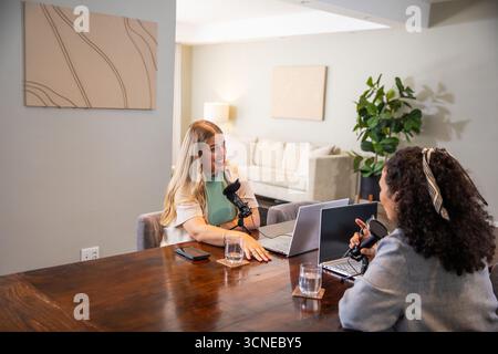 Verschiedene weibliche Kollegen, die am Wohnzimmertisch mit Laptops und Mikrofonen aufzeichnen Stockfoto