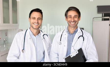 Zwei lächelnde Ärzte stehen in der Klinik und schauen in die Kamera Stockfoto