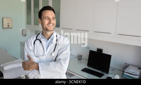 Lächelnder, selbstbewusster Arzt, der mit gekreuzten Armen im Büro steht Stockfoto