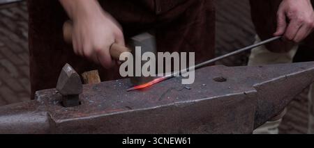 ROTTERDAM, NIEDERLANDE - 13. SEPTEMBER 2025 - Schmied hämmert glühende Metallstäbe auf einen schweren Amboss und formt Eisen mit traditionellem Handwerk Stockfoto