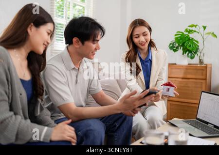 Professionelle asiatische Immobilienmakler berät glückliche Erwachsene Paare zu Hause. Erörterung neuer Immobilieninvestitionspläne für Immobilienoptionen. Bequemes Meet Stockfoto