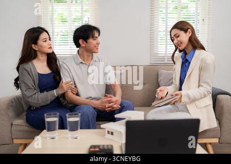 Immobilienmakler erklärt asiatischen Paaren zu Hause Immobilienoptionen. Sie diskutieren über Zukunftspläne für Wohnungsbauinvestitionen und Hypothekenberatung. Comforta Stockfoto