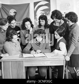 Junge Arbeiter nehmen in den 1970er Jahren an einem Treffen der Komsomol (Junge Kommunistische Liga) in der „Roten Ecke“ im AIZ-Werk in Sloviansk, UdSSR Teil Dieses Schwarzweiß-Archivfoto zeigt die Szene der Unterzeichnung eines wichtigen Dokuments vor dem Hintergrund sowjetischer Plakate und des Komsomol-Banners, das die Atmosphäre des ideologischen und sozialen Lebens der sowjetischen Jugend vermittelt Stockfoto