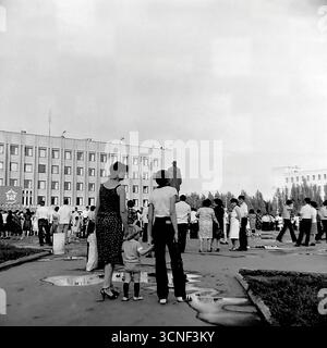 Bewohner und Familien mit Kindern spazieren während des Stadtfestes in Sloviansk, UdSSR, am 6. September 1985 durch den zentralen Platz der Oktoberrevolution (heute Soborna-Platz) in der Nähe des Lenin-Denkmals. Dieses authentische Schwarzweiß-Reportage-Foto fängt die lebhafte Atmosphäre eines öffentlichen Festivals und einer Massenveranstaltung ein, bei der die Menschen trotz der Pfützen eines früheren Regens gemeinsam den Urlaub genießen und eine typische Szene des bürgerlichen Lebens in der Sowjetzeit darstellen Stockfoto
