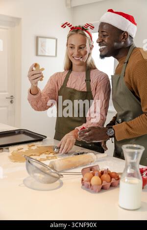 Diverse Paare mit Schürzen Weihnachtsmützen Formen Keksenteig mit rollenden Nadelschneidern Stockfoto