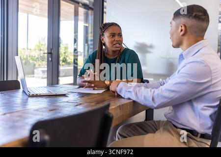Verschiedene Kollegen in Geschäftskleidung diskutieren, offene Laptops sehen, Dokumente am Konferenztisch Stockfoto