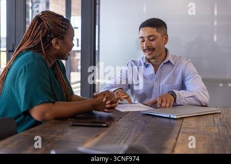 Verschiedene Kollegen sitzen am rustikalen Holztisch im Büro und diskutieren Dokumente per Smartphone Stockfoto