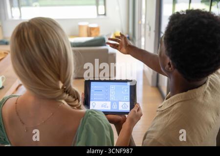 Verschiedene Paare stehen und diskutieren über Smart-Home-Steuerungen im Wohnzimmer mithilfe eines Tablets Stockfoto