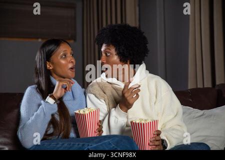 Verschiedene Paare sitzen dicht zusammen auf einer dunklen Couch zu Hause, gestreifte Popcorn-Behälter Stockfoto