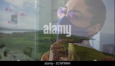 Eine Frau mit Maske und Brille, die das Kinn über Ackerland und Küstenbucht berührt, Kopierraum Stockfoto