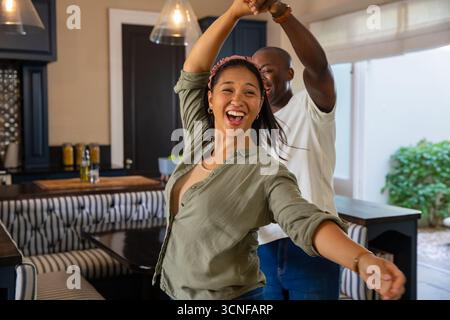 Verschiedene Paare tanzen in der Küche um die gestreifte Bank und den Esstisch unter Glaslichtern Stockfoto