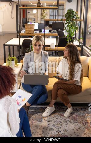 Verschiedene weibliche Kollegen diskutieren Projektpläne und Laptop-Details in der Bürolounge Stockfoto