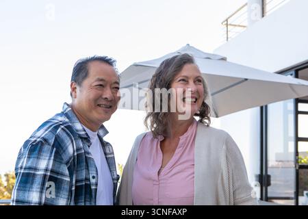 Verschiedene Seniorenpaare stehen auf dem Balkon am Geländer unter dem Sonnenschirm und lächeln Stockfoto