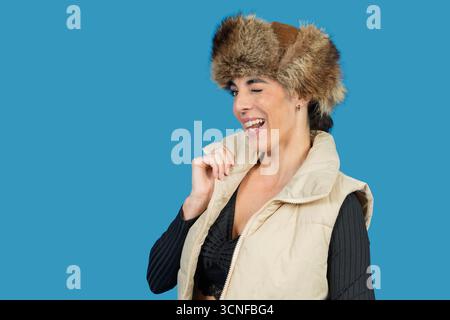 Frau, die zuzwinkert, lacht, Winterkleidung trägt, eine fröhliche Einstellung zeigt Stockfoto