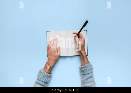 Ein leeres Notizbuch auf neutralem Hintergrund mit Händen in Schreibposition. Ein Symbol für Planung, Kreativität und für Themen wie Back to School und Bulle Stockfoto