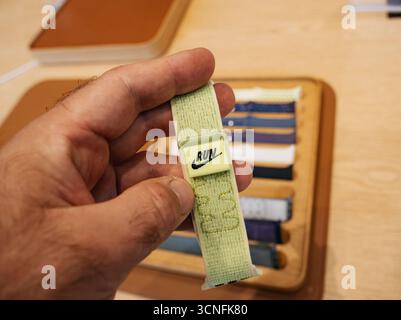 Nahaufnahme einer Hand, die das neue Nike Apple Watch Ultra 3 Band aus Stoff hält, mit LAUFLOGO im Apple Store und Zubehör auf der Rückseite Stockfoto