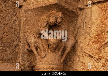 Zwei lachende Tiere, jedes mit Pferdekopf und Mähne, aber mit Klauenfüßen statt Hufen, halten einen menschlichen Kopf herunter. Spätmittelalterliche Hauptstadt, die im 12. Jahrhundert n. Chr. erbaut wurde, im Eingangsportal des Benediktinerkrankenhauses oder Hospizes Besalú, Katalonien, Spanien. Stockfoto