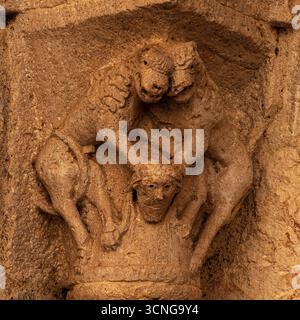 Zwei Hybridtiere, jedes mit Pferdekopf und Mähne und Klauenfüßen statt Hufen, scheinen lachend zu sein, wenn sie mit ihren Klauen einen menschlichen Kopf niederhalten. Spätmittelalterliche Hauptstadt, die im 12. Jahrhundert n. Chr. erbaut wurde, im Eingangsportal des Benediktinerkrankenhauses oder Hospizes Besalú, Katalonien, Spanien. Stockfoto