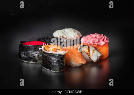 Verschiedene Sushi-Brötchen auf dunkler Oberfläche. Umfasst verschiedene Arten von Sushi mit farbenfrohen Belägen und Nori-Wraps. Perfekt für Restaurant m Stockfoto