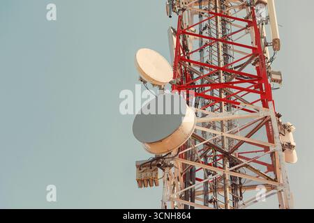 Telekommunikationsturm mit Mikrowellenantennen, der an klaren, sonnigen Tagen Daten nahtlos vor einem leuchtend blauen Himmel überträgt Stockfoto