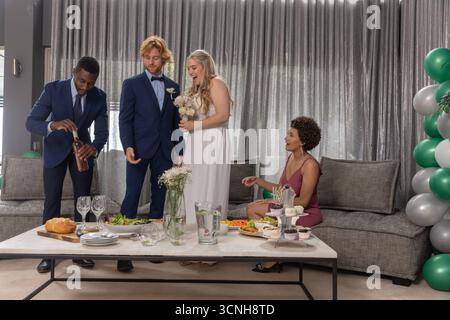 Vielfältige Hochzeitsfeier in Hochzeitskleidung mit Weingläsern, mit Blumenstrauß in der Lounge Stockfoto
