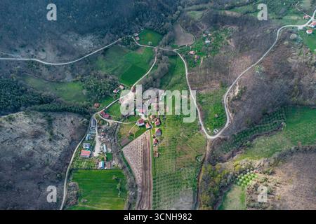 Drohne fängt die ruhige Schönheit eines kleinen Dorfes ein, eingebettet in sanfte Hügel, gewundene Straßen und lebhafte grüne Felder Stockfoto