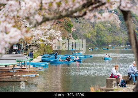 Kyoto, Japan - 10. April 2025 : Touristen, die auf traditionellen Sportbooten auf dem Katsura-Fluss in der Nähe der Togetsukyo-Brücke in Arashiyama fahren. Stockfoto