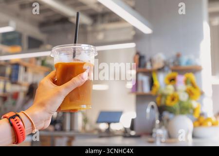 Frau, die Eiskaffee in einem Plastikbecher mit Strohhalm in einem Café hält und ein erfrischendes Getränk genießt Stockfoto
