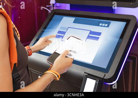 Frau scannt Barcode am Selbstbedienungskiosk mit Touchscreen mit Smartphone und gedrucktem Beleg Stockfoto