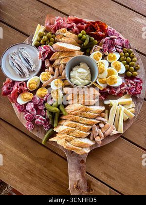 Verschiedene Wurstplatten mit Wurstwaren, Käse, Brot, Oliven, Eiern, Sardellen, Gurken und Mayonnaise werden auf einem Holzbrett serviert. Stockfoto