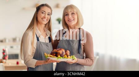 Glückliche Millennials-Frau mit ihrer älteren Mutter, die traditionellen truthahn hält und Weihnachten oder Thanksgiving-Dinner vorbereitet Stockfoto