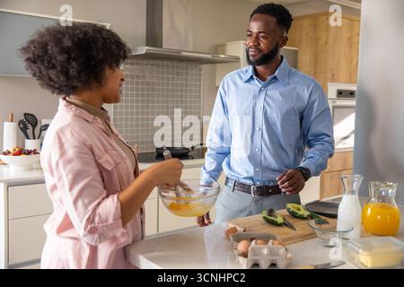 Diverse Paare in Business-Freizeitkleidung, die Eier in einer Schüssel auf der Kücheninsel mit Avocados rasten Stockfoto