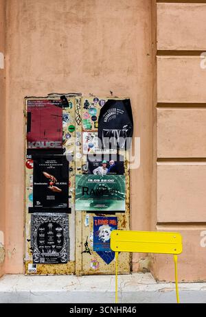 Plakate und Aufkleber an einer Wand in Tartu, Estland, werben für Theater, Konzerte und Kunstveranstaltungen. Ein gelber Stuhl sorgt für urbanen Kontrast. Stockfoto