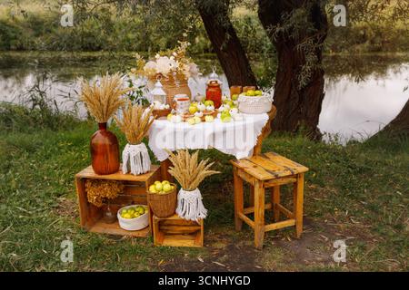 Herbst mit einem dekorierten Tisch im Freien an einem ruhigen Gewässer. Der Tisch, mit einem weißen Tuch bedeckt, ist mit einem schönen Erntelöffel beladen Stockfoto