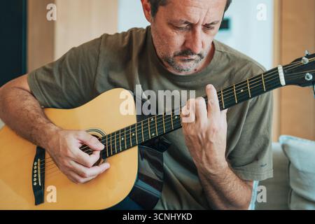 Amateurmusiker, der zu Hause Akustikgitarrenspiele, lässiges Lifestyle und kreatives Konzept übt und lernt. Selektiver Fokus. Stockfoto