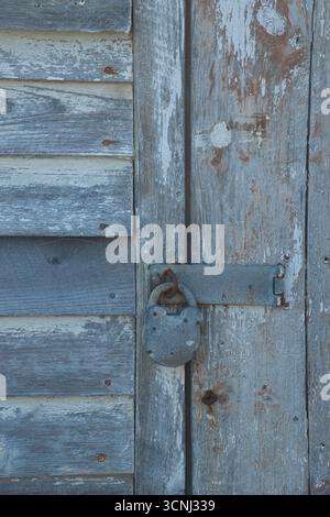 Die Holztür, die in Blau- und Grautönen gestrichen ist, verfügt über ein rostiges Schloss, das einen Einblick in die Geschichte dieses verlassenen Ortes gibt, was die Highlights hervorhebt Stockfoto