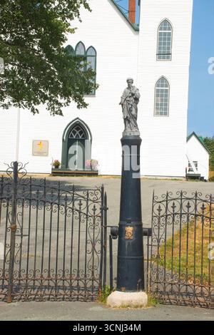 Eine Statue eines heiligen steht auf einem Kanon neben einem schmiedeeisernen Tor, das an die Kirche St. Peter und Paul in Bay Bulls, Neufundland, grenzt Stockfoto