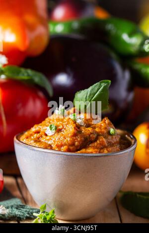 Auberginen-Kaviar in einem Glas und Gemüse auf hölzernem Hintergrund. Stockfoto