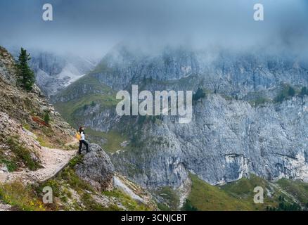 Frau mit Rucksack steht auf felsigem Weg in den Bergen im Nebel Stockfoto
