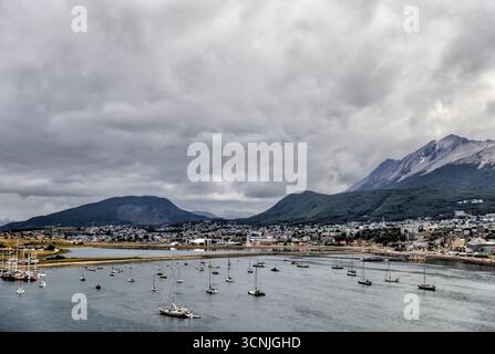 Ein Panoramablick auf den ruhigen Hafen in Ushuaia, der südlichsten Stadt der Welt, mit angedockten Schiffen, Fischerbooten und einem dramatischen, bedeckten Himmel Stockfoto