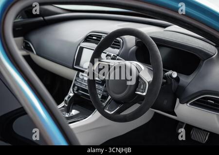 Moderner Innenraum mit hellem beigefarbenem Leder. Fahrersitz eines blauen Luxusautos mit Rechtslenkung: Lenkrad, Armaturenbrett und Mittelkonsole. Stockfoto