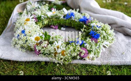 Die aus lebendigen Wildblumen und Grün gefertigte Blumenkrone liegt auf weichem Stoff und repräsentiert eine traditionelle Feier während der Sonnenwende Stockfoto
