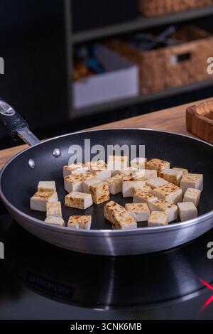 Goldbraune Tofuwürfel in einer antihaftbeschichteten Pfanne auf einem modernen Herd zwitschern den Kochprozess und sorgen für eine einladende Küchenatmosphäre Stockfoto