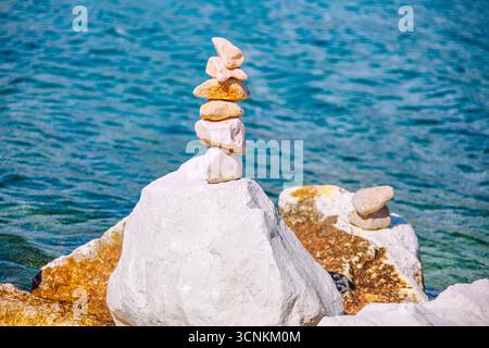 Perfekt ausbalancierter Steinkairn steht widerstandsfähig gegen das ruhige blaue Meer und symbolisiert Frieden und Harmonie. Ein ruhiges Bild sorgt für eine beruhigende Note Stockfoto