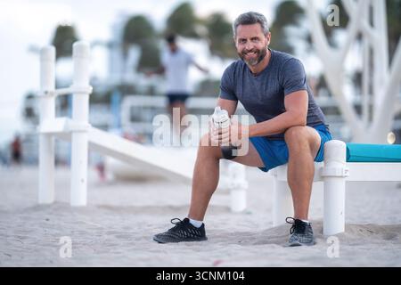 Sport-Fitness-Mann, der draußen auf einer Bank ruht. Reifes Fitnesssportmodell, das nach dem Training auf einer Bank sitzt. Ein Sportmann macht nach dem Fitnesstraining eine Pause Stockfoto