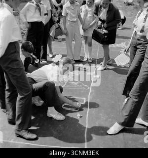 Ein stimmungsvolles Schwarzweiß-Foto fängt eine Kreidezeichnung auf Asphaltkonkurrenz in Sloviansk in den 1970er Jahren ein; eine Gruppe sowjetischer Pioniere in Schuluniformen erstellt enthusiastisch große patriotische Zeichnungen zu den Themen Raum, Frieden und Heldentum unter der Aufsicht von Lehrern, was ein klassisches Beispiel für kollektive Kreativität und ideologische Erziehung von Kindern in der UdSSR ist Stockfoto
