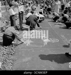 Ein stimmungsvolles Schwarzweiß-Foto fängt eine Kreidezeichnung auf Asphaltkonkurrenz in Sloviansk in den 1970er Jahren ein; eine Gruppe sowjetischer Pioniere in Schuluniformen erstellt enthusiastisch große patriotische Zeichnungen zu den Themen Raum, Frieden und Heldentum unter der Aufsicht von Lehrern, was ein klassisches Beispiel für kollektive Kreativität und ideologische Erziehung von Kindern in der UdSSR ist Stockfoto