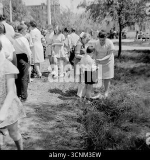 Ein stimmungsvolles Schwarzweiß-Foto fängt eine Kreidezeichnung auf Asphaltkonkurrenz in Sloviansk in den 1970er Jahren ein; eine Gruppe sowjetischer Pioniere in Schuluniformen erstellt enthusiastisch große patriotische Zeichnungen zu den Themen Raum, Frieden und Heldentum unter der Aufsicht von Lehrern, was ein klassisches Beispiel für kollektive Kreativität und ideologische Erziehung von Kindern in der UdSSR ist Stockfoto