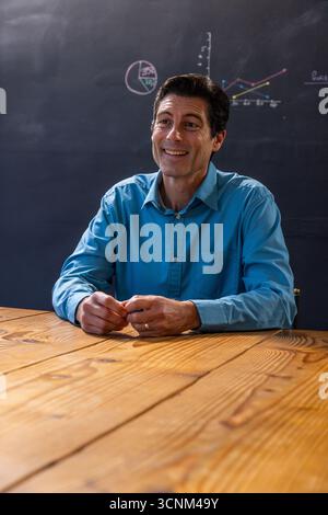 Männlicher Dozent mit Tisch und Tafel mit Torten- und Liniendiagrammen im Klassenzimmer Stockfoto